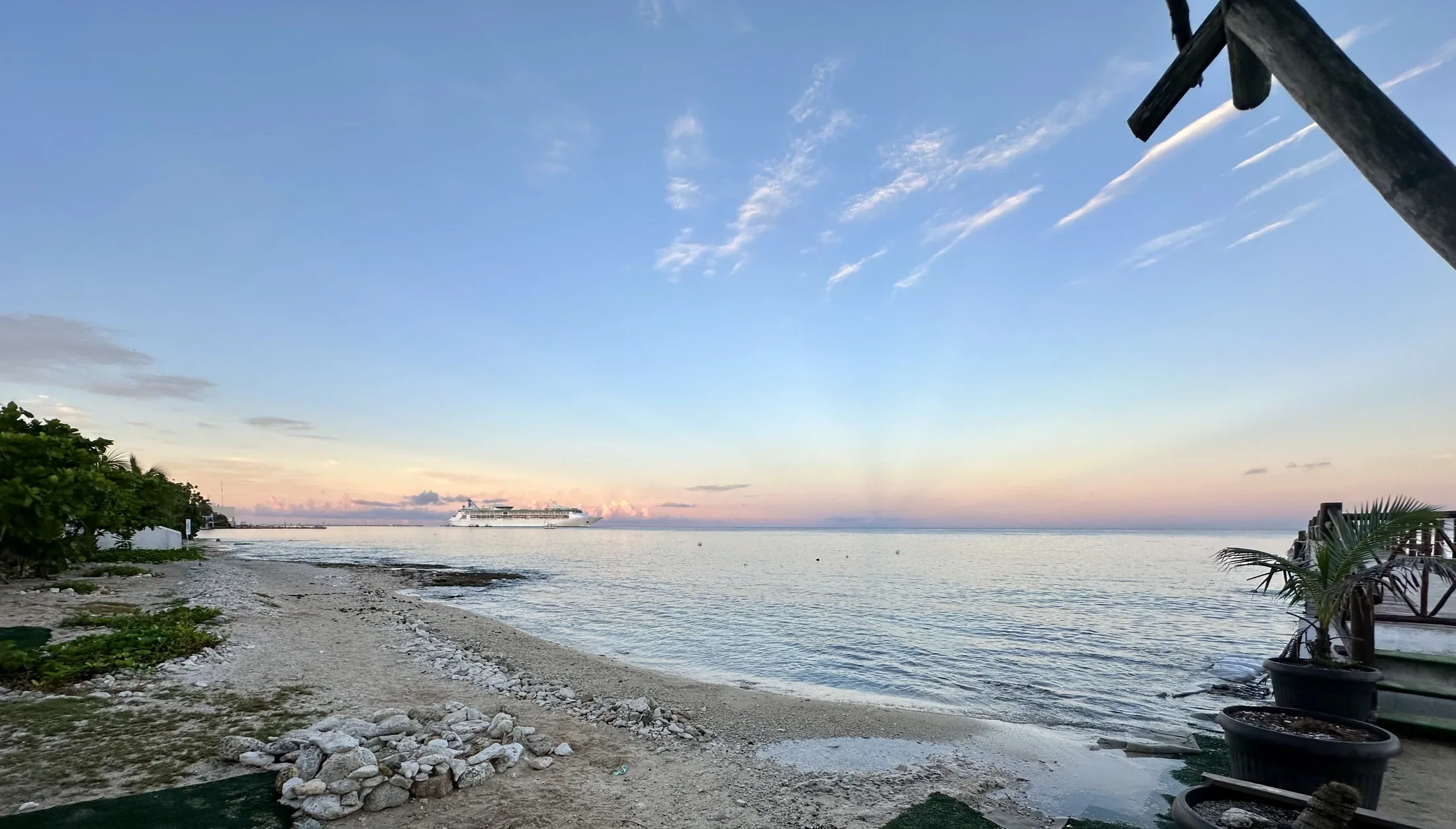 A calm Cozumel shoreline with a cruise ship offshore in the soft evening light.